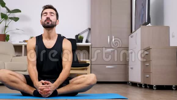 年轻的健身男子做瑜伽莲花姿势在他的地板上视频的预览图