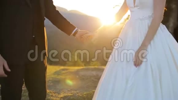 新婚夫妇手牵手在日落背景拍摄慢动作美丽的山峦视频的预览图