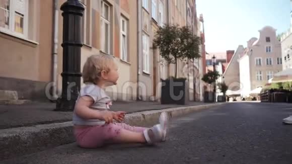 坐在路上走在街上的金发小女孩视频的预览图