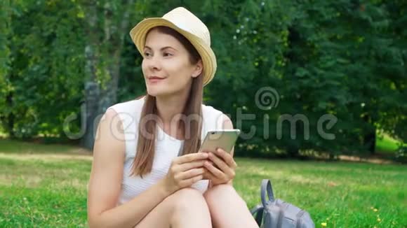 女学生用手机坐在大学校园的草地上公共公园的游客用手机聊天视频的预览图
