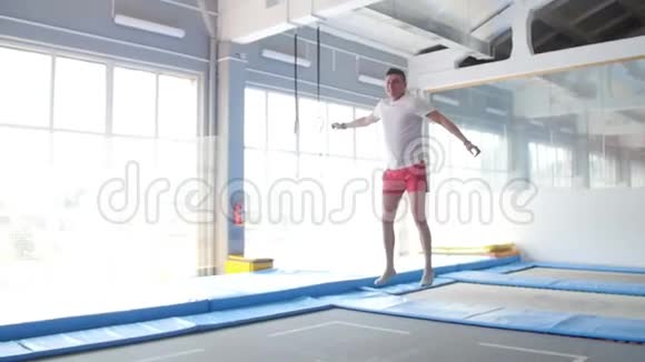 健身娱乐理念一个年轻健康的快乐男人在蹦床上跳跃视频的预览图