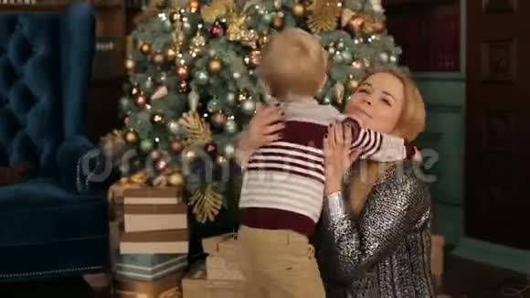 妈妈轻轻地抱着小儿子靠近圣诞树视频的预览图