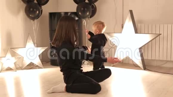 一个年轻快乐的妈妈正在和她一岁的男孩在一个有星星的工作室里玩视频的预览图