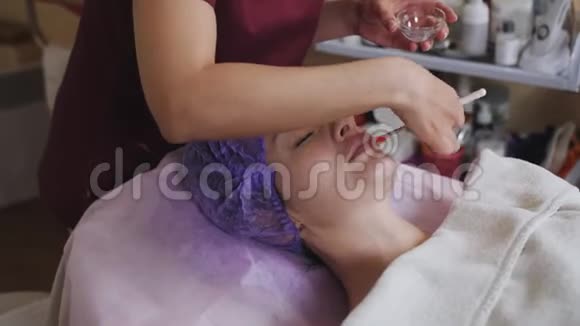 美容中心的年轻女性客户做护肤手术手套中的美容师用刷子涂抹医用酸视频的预览图