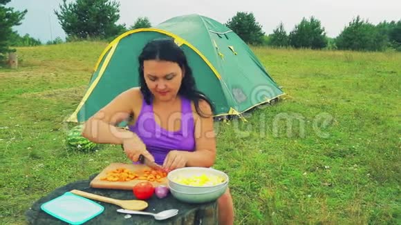 一个女人在帐篷附近的森林里把胡萝卜切成薄片放在一张放蔬菜的木桌上视频的预览图