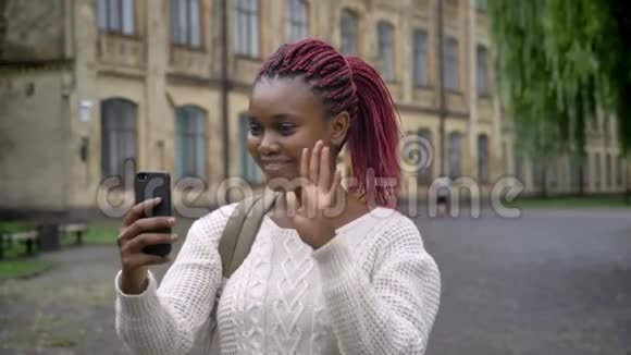 美丽的年轻非洲女学生通过电话视频聊天站在大学附近的公园里微笑视频的预览图