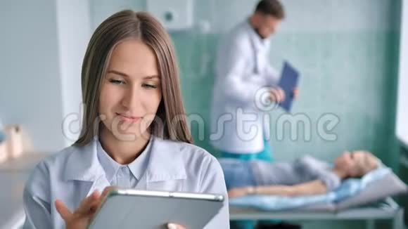 用PC平板电脑为病人准备手术用白色实验室外套微笑女医生视频的预览图