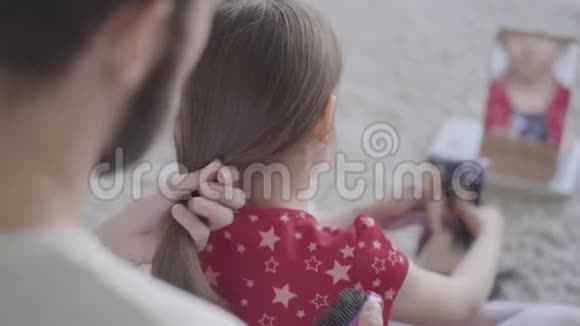 小胡子的父亲正在给小女孩梳头而孩子则在毛茸茸的地上梳理玩具视频的预览图