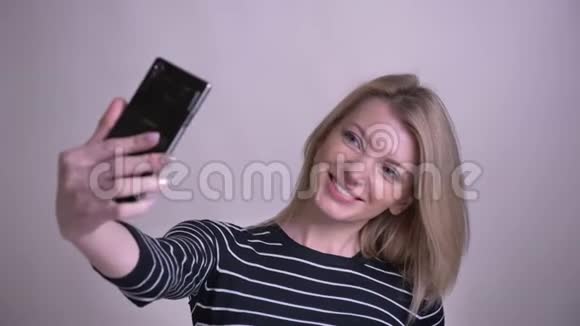 一幅成年金发白种人女性在手机上自拍的特写照片照片背景带着微笑视频的预览图