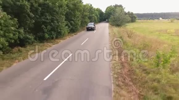 一辆黑色的大轿车正行驶在乡间公路上人们正驾车从无人驾驶飞机上射击视频的预览图