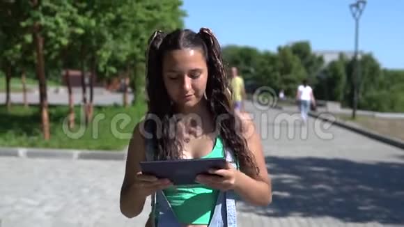 一个漂亮的女孩正在公园里用平板电脑走路慢动作视频的预览图