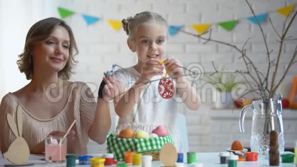 妈妈和女儿用手工玩具装饰树枝复活节传统视频的预览图