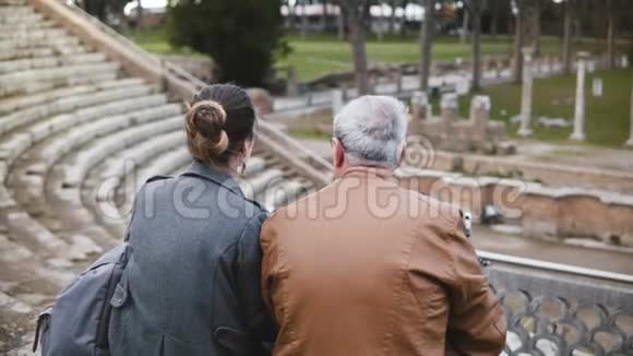 在意大利古老的奥斯蒂亚圆形剧场废墟上坐着交谈的欧洲父女的后景视频的预览图