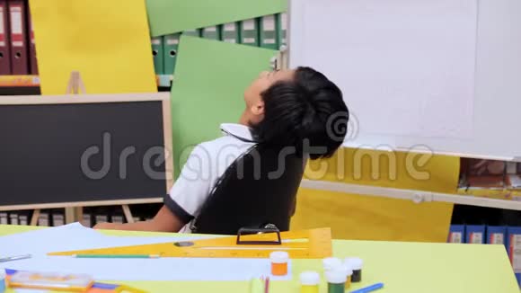 一个男孩坐在椅子上在一张桌子旁边放着书写用具视频的预览图