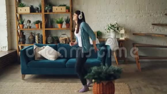 快乐的年轻女子正在家里跳舞通过耳机听音乐玩得开心享受空闲时间现代视频的预览图
