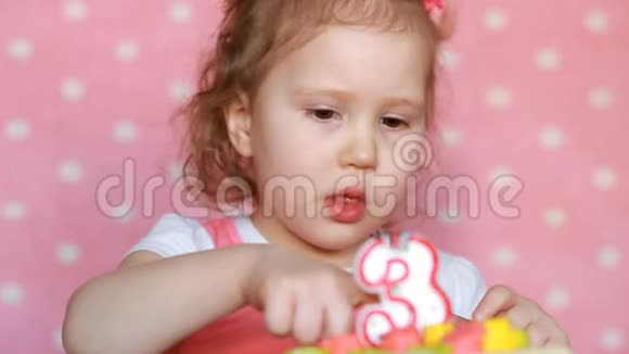 一个有趣的小女孩吃了一个美味的蛋糕来纪念他的生日三年一个孩子在一张粉红色的桌子上吃甜点视频的预览图
