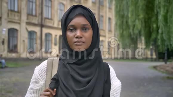 年轻的穆斯林非洲学生戴着头巾背着背包对着镜头微笑站在大学附近的公园里视频的预览图