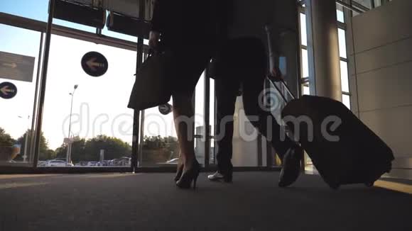 商人带着他的女同事通过玻璃门离开候机楼并用轮子滚动手提箱商业人士视频的预览图