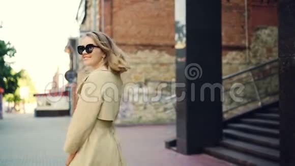 慢镜头描绘了一位穿着优雅服装微笑着看着镜头走在街上的幸福年轻女士视频的预览图