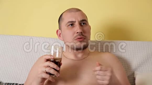 秃头的胖子躺在沙发上看电视吃薯条和可口可乐视频的预览图