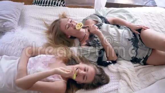 母鸡派对穿丝绸睡衣的姐妹们吃甜棒棒糖躺在家里的床上聊天视频的预览图