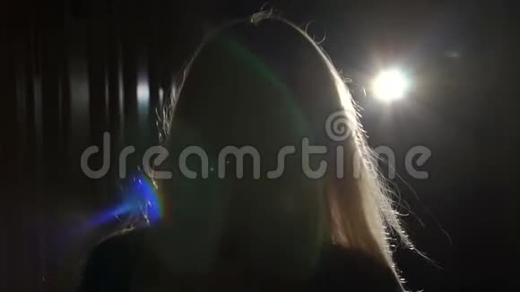 头发飞扬的女孩在黑暗中站在明亮的聚光灯下视频的预览图