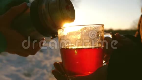 冬天人们在夕阳下把热水瓶里的热茶倒进玻璃酒杯里女孩拿着一杯茶视频的预览图