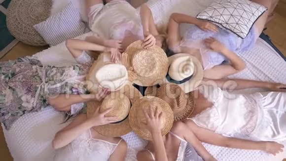 派对上女孩们穿着睡衣脸上戴着草帽躺在床上然后脱下它们在室内对着镜头微笑视频的预览图