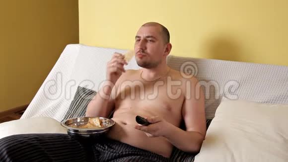 懒洋洋的秃头的胖乎乎的没有外套的胖子正在看电视在沙发上喝着薯片的可口可乐胖子视频的预览图
