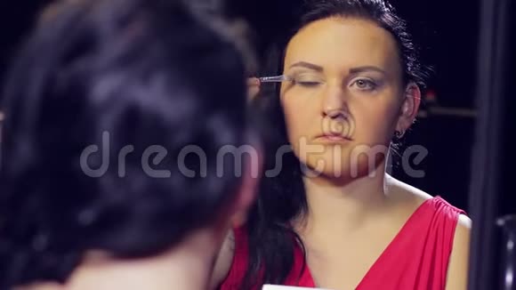 一个年轻的黑发女人穿着一件红色的裙子在镜子前用刷子涂上浅色的眼妆视频的预览图