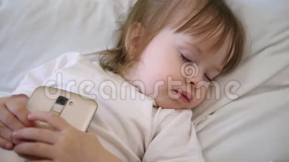 可爱的婴儿睡在床上智能手机孩子躺在枕头上拿着一块药片视频的预览图