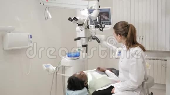 牙医把现代显微镜对准病人漂亮的女医生牙医年轻的非裔美国男性视频的预览图