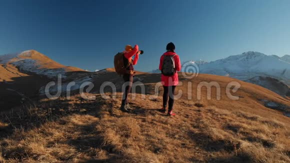 两个带背包和照相机的旅行女孩在山上漫步在史诗般的岩石之间的空中景色视频的预览图