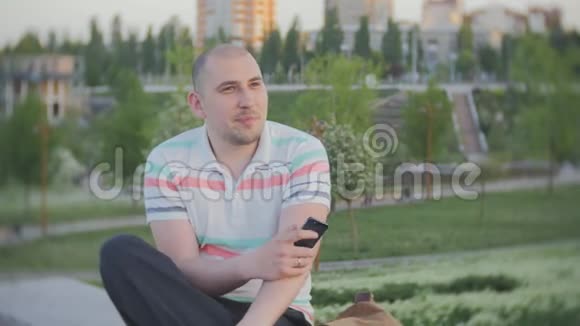 年轻人坐在广场上拿着他的智能手机视频的预览图