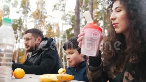 妈妈爸爸和孩子在餐桌旁的树林里坐在一起享受美食前景关注重点视频的预览图