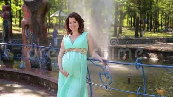 一个穿着长裙的怀孕女孩站在喷泉背景下的城市公园里视频的预览图