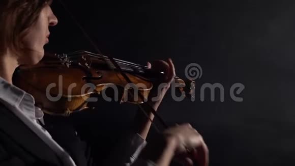 黑暗工作室一个音乐家拉小提琴同时站在他的背黑烟背景背面视频的预览图