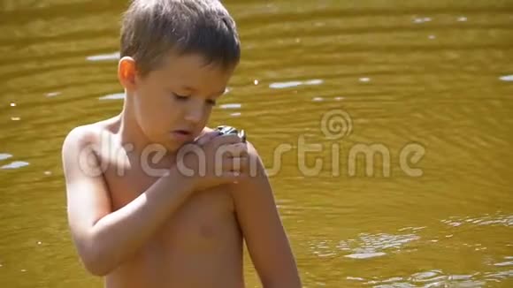 蟾蜍坐在河边海滩上的一个年幼的孩子的肩膀上慢动作视频的预览图