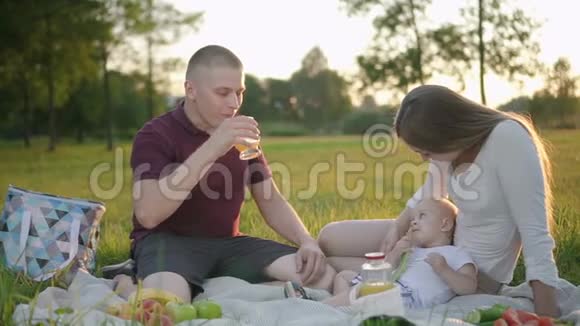 带着婴儿的美国年轻家庭坐在绿色公园野餐视频的预览图