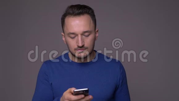 年轻英俊的白种人的特写镜头他在电话里发短信背景是灰色的视频的预览图