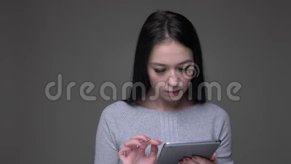 在平板电脑上发短信的白种人年轻漂亮的女性特写镜头看着背景隔离的相机视频的预览图