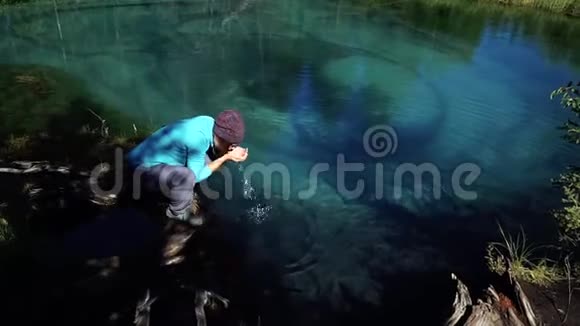 一位戴着背包帽子的年轻游客正在从冰冷的蓝山湖喝水视频的预览图