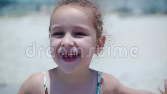 一个穿着泳装的迷人小女孩的肖像一个孩子微笑着站在沙滩上看着摄像机视频的预览图