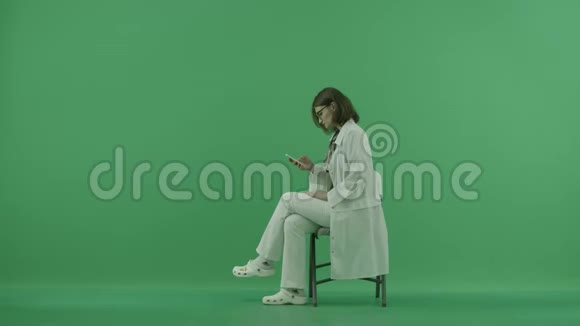 医生坐在椅子上在绿色屏幕上的手机里找东西视频的预览图