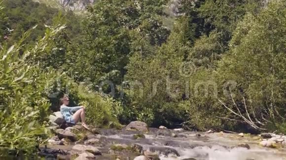 湍急的河流在山林中流淌在河岸休息的女游客视频的预览图