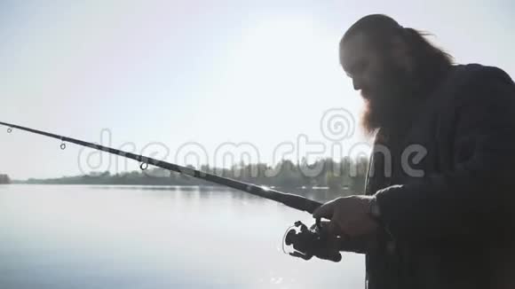大胡子渔夫调整钓竿费舍尔准备钓鱼在河上钓鱼视频的预览图