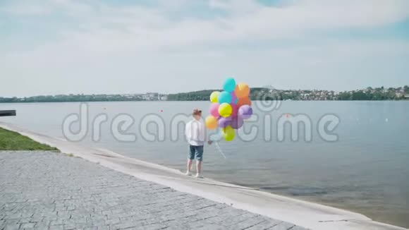 快乐的小男孩站在湖岸上手里拿着五颜六色的气球4K视频的预览图