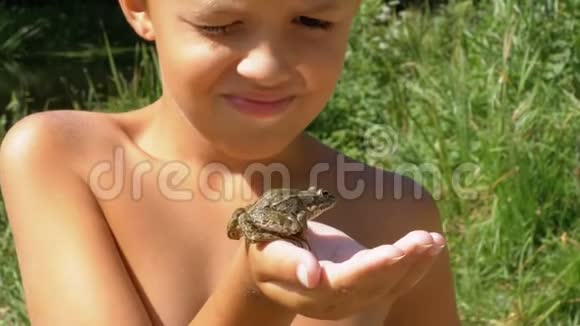 小男孩手里拿着一只青蛙用手指在河边的海滩上抚摸他的蟾蜍视频的预览图