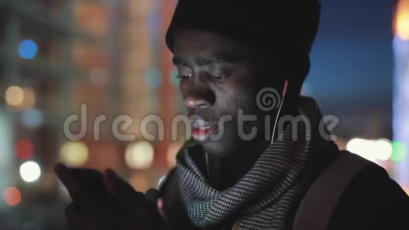 非洲男人夜间在耳机里使用智能手机视频的预览图