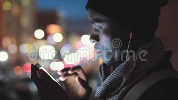 非洲男人夜间在耳机里使用智能手机视频的预览图